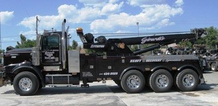 Black heavy-duty tow truck parked on a paved lot under a sunny sky.