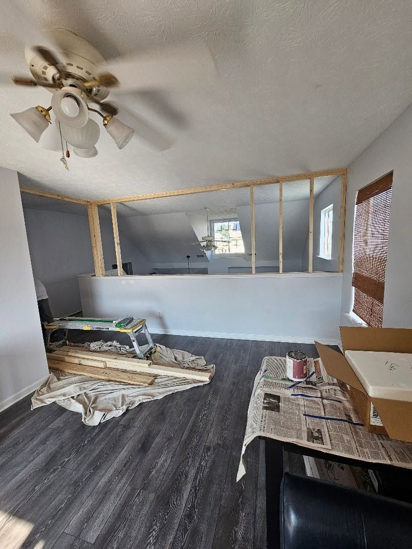 Living room with gray walls, dark flooring, ceiling fan, and a partial room divider under construction