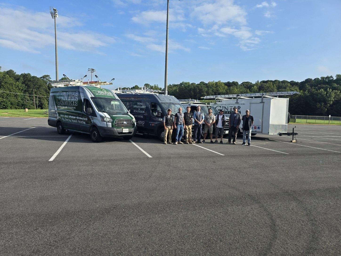 Group of people standing beside two dark vans in a parking lot on a sunny day