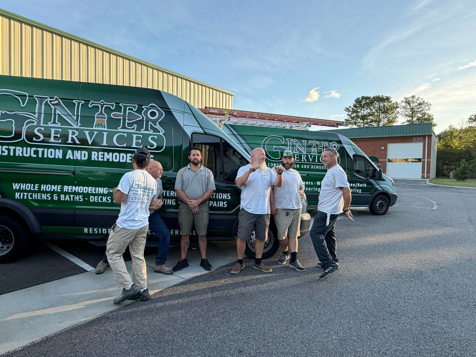 Five workers stand in front of a green construction van in a parking lot, smiling and posing