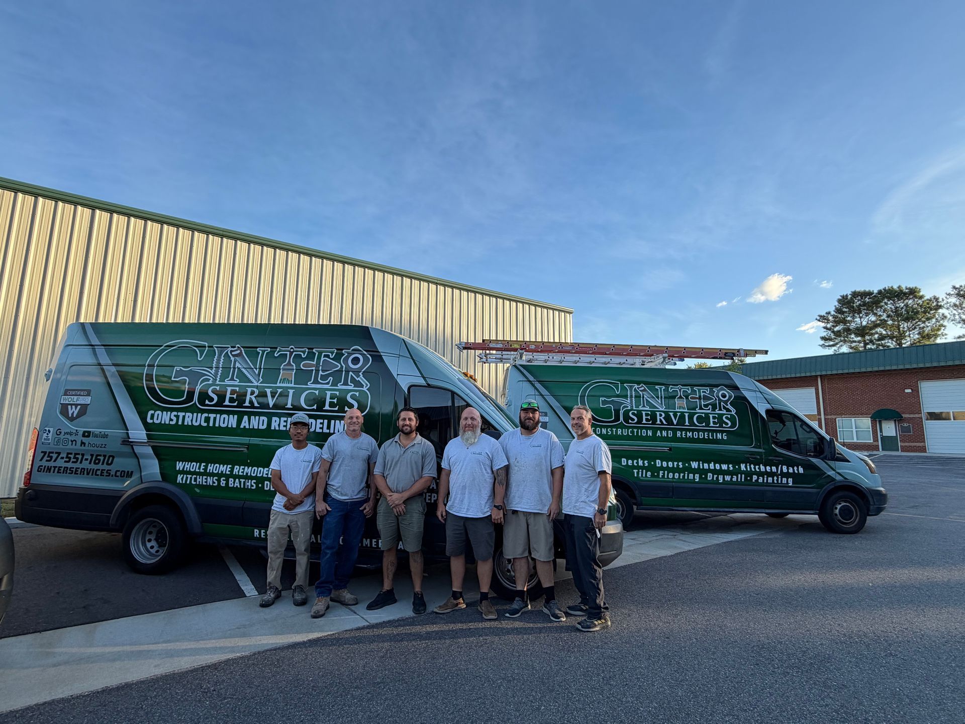 Group of workers posing in front of two green service vans outside a warehouse.