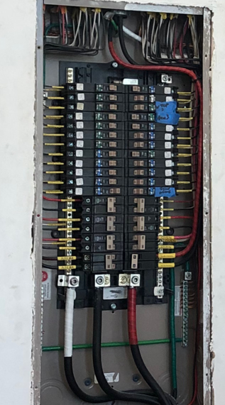 Open electrical breaker panel with rows of circuit breakers and colored wires.
