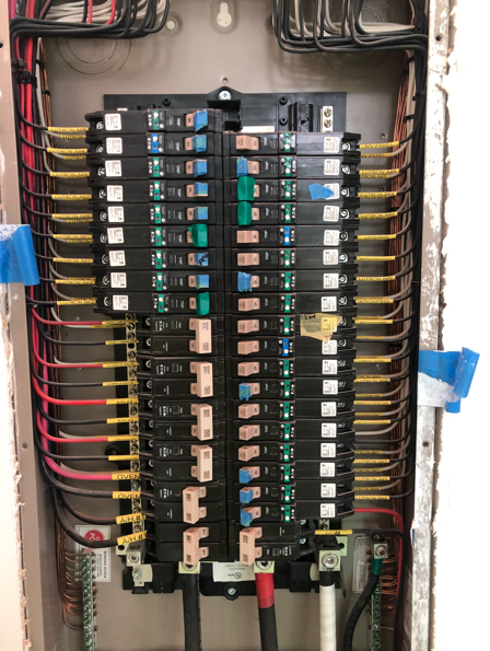 Electrical breaker panel with rows of circuit breakers and bundled wires in a utility cabinet