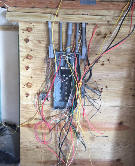 Open electrical breaker panel with tangled red, yellow, and black wires inside wooden framing