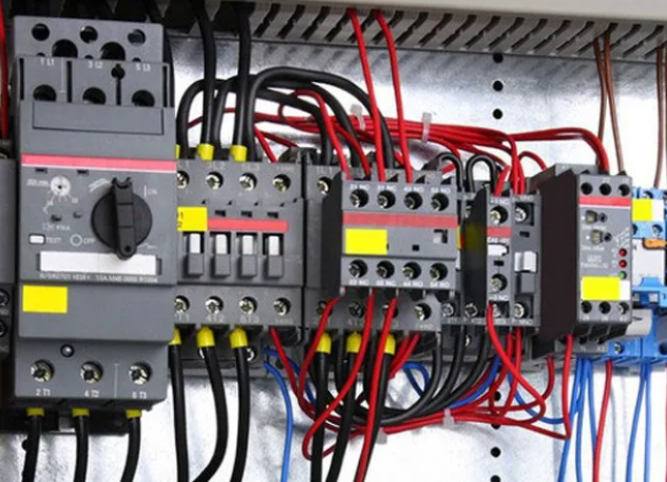 Electrical control panel with relays, switches, and red and black wiring.