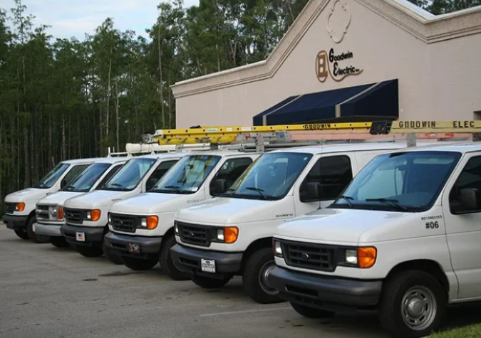 Row of white service vans parked outside a building with a sign, some with ladders on top