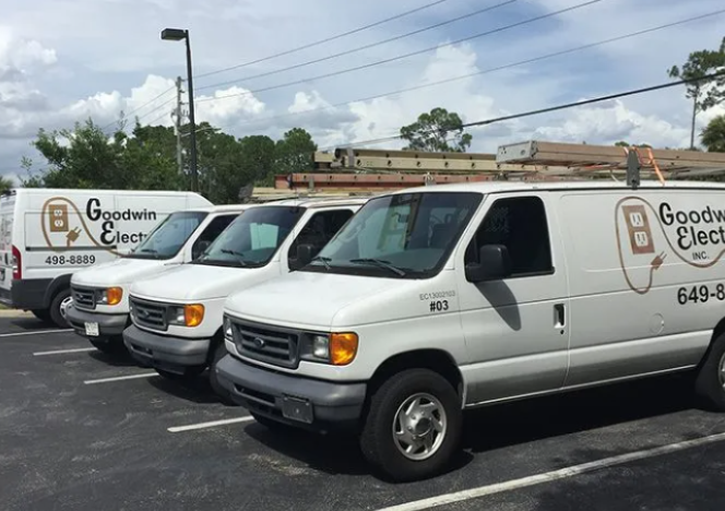 White Goodwin Electric service vans parked in a lot under a cloudy sky.