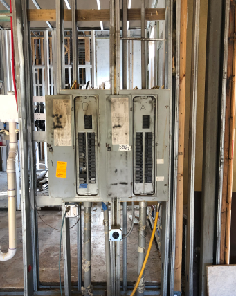 Old electrical breaker panel mounted on exposed studs in a construction site wall