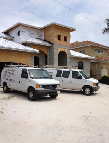 Two white service vans parked in front of a large stucco house under construction.