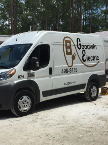 White Goodwin Electric service van parked outdoors among pine trees.