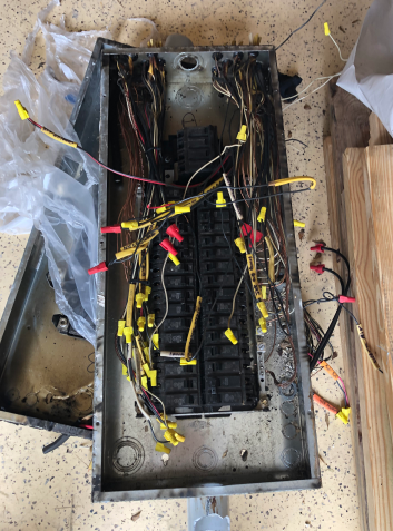 Open metal electrical box with tangled wires, yellow connectors, and debris inside on a dirty floor