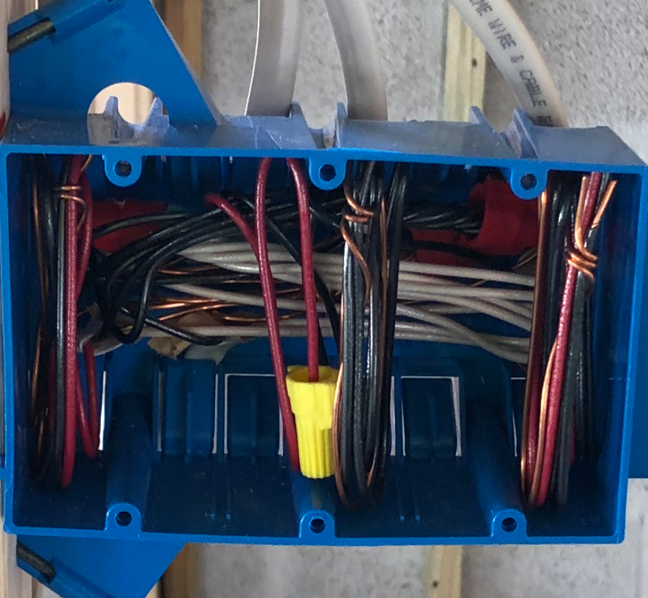 Blue electrical junction box with red and gray wires, showing a yellow wire nut inside