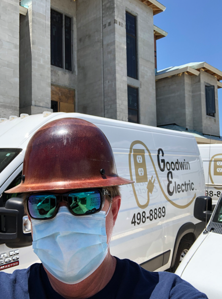Worker in hard hat and mask in front of a Goodman Electric van at a construction site