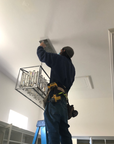 Worker on a ladder installing a ceiling fixture in a room