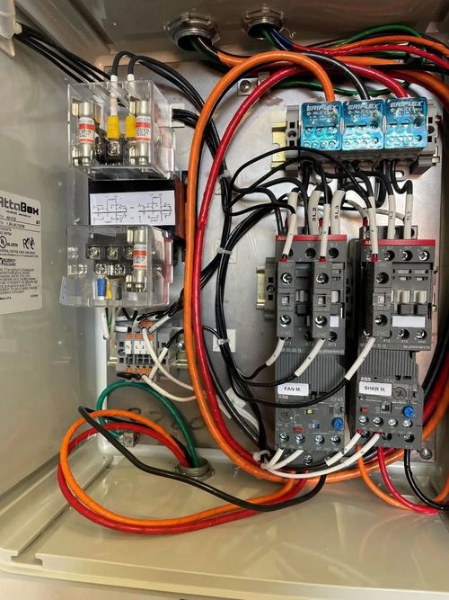 Open electrical control panel with wiring, relays, breakers, and red, black, and green cables