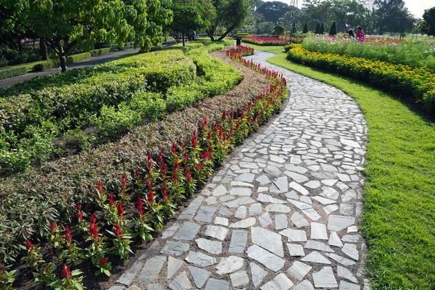 Curving stone path through a colorful flower garden with green hedges and trees