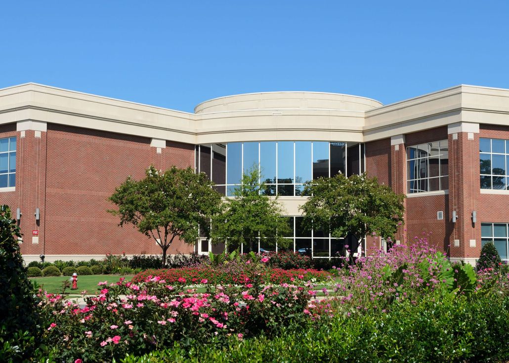 Modern brick building with curved glass entrance and flower garden under a blue sky