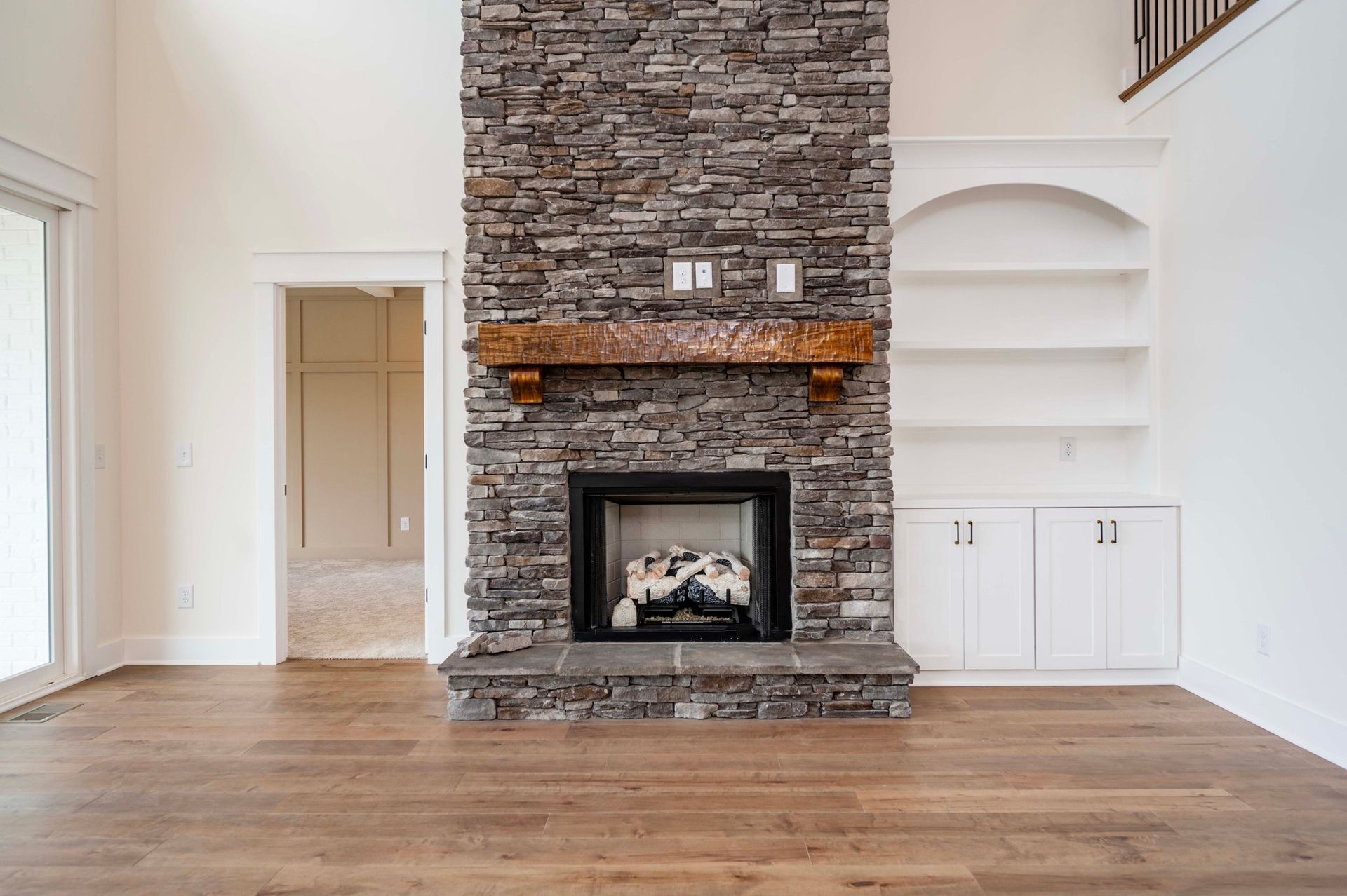 Stone fireplace with wooden mantel, built-in shelves and cabinets, in a room with hardwood floors.