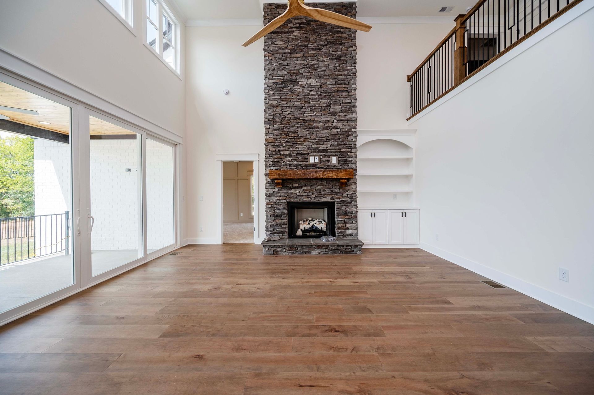 Spacious living room with stone fireplace, wooden floors, and large windows.