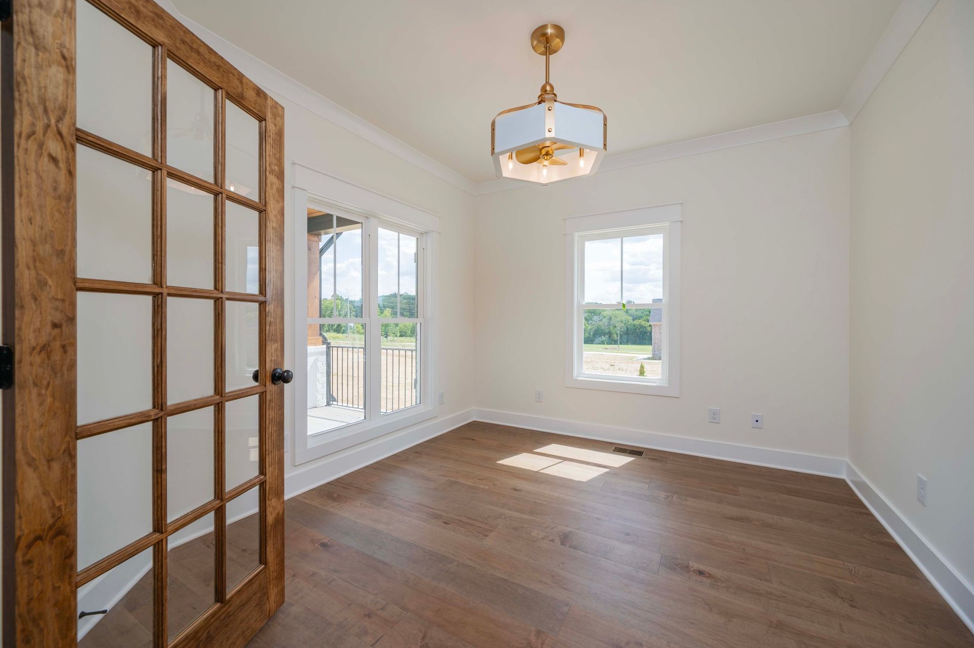 Empty room with hardwood floors, white walls, and a decorative ceiling light. Wooden door and windows.