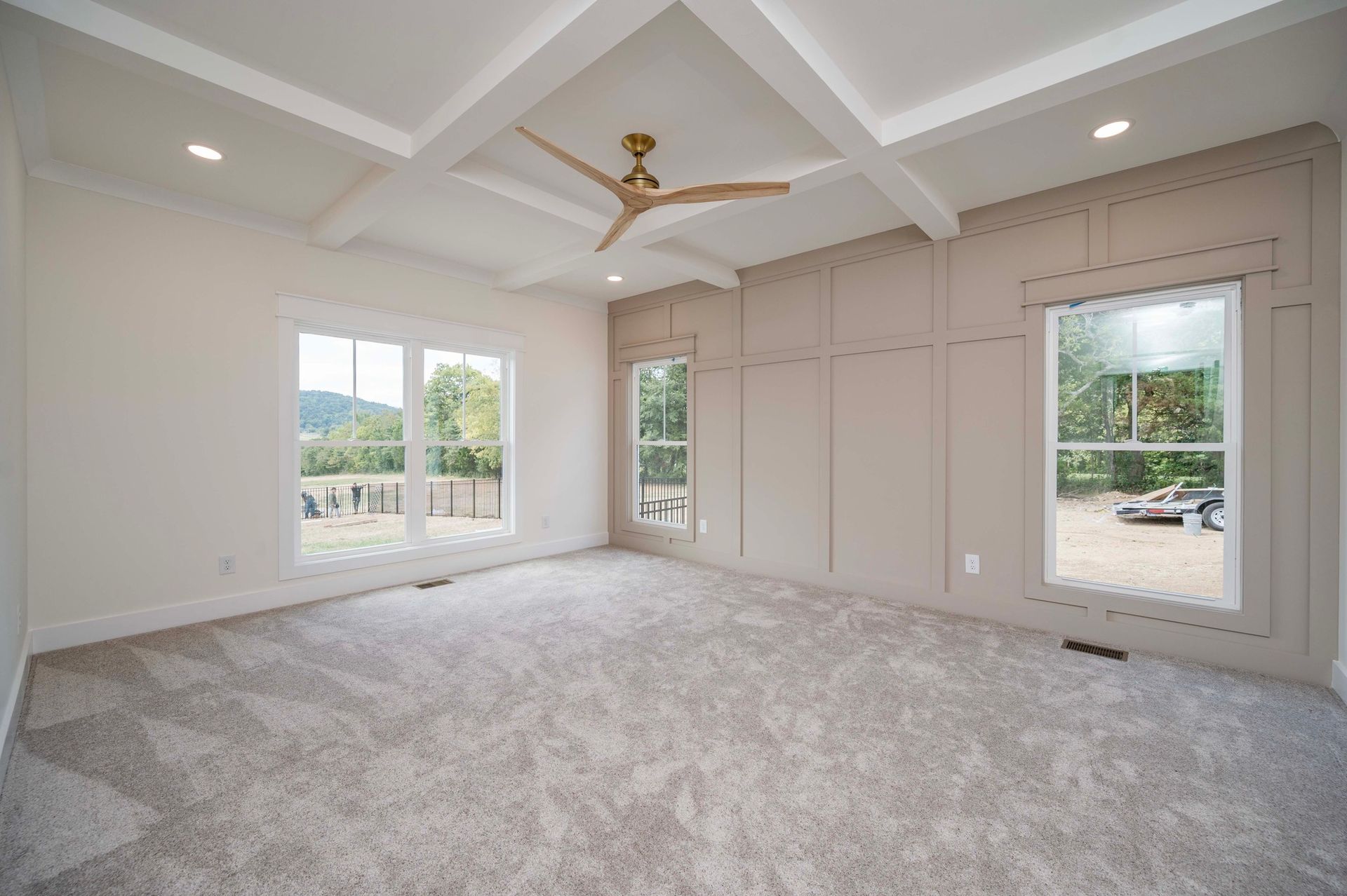 Empty bedroom with light gray carpet, windows, and coffered ceiling.