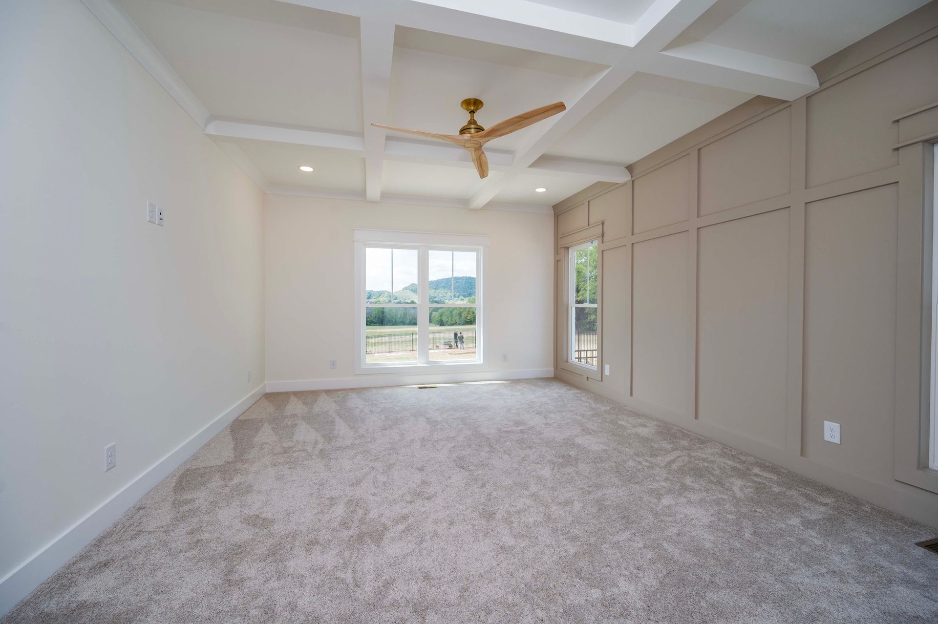 Empty bedroom with beige walls, white trim, and a window overlooking a green landscape.