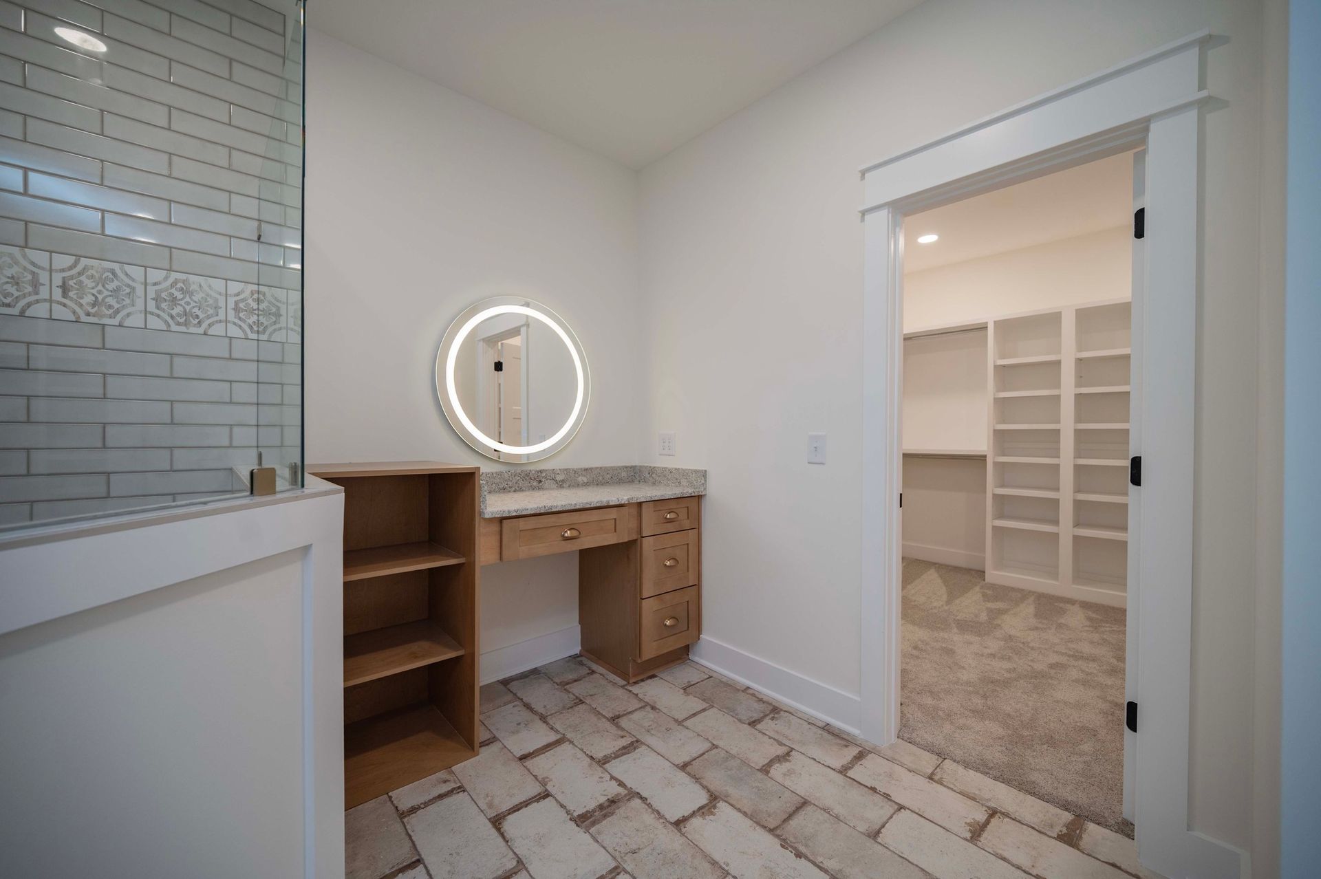 Bathroom with vanity, built-in shelves, and a walk-in closet. Light wood, white walls, and brick-style floor.