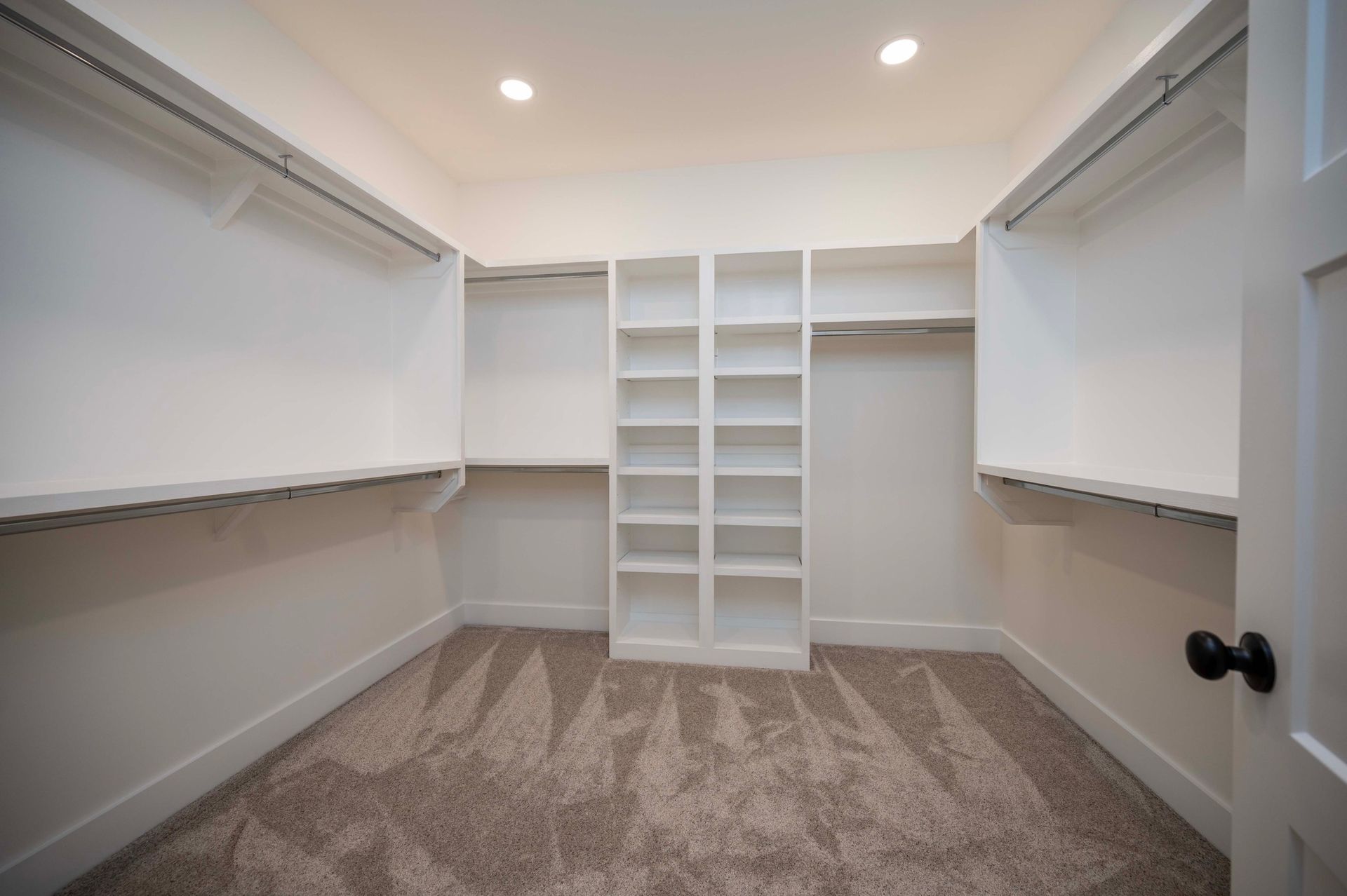 Empty white closet with built-in shelves and rods, tan carpet, and white door.