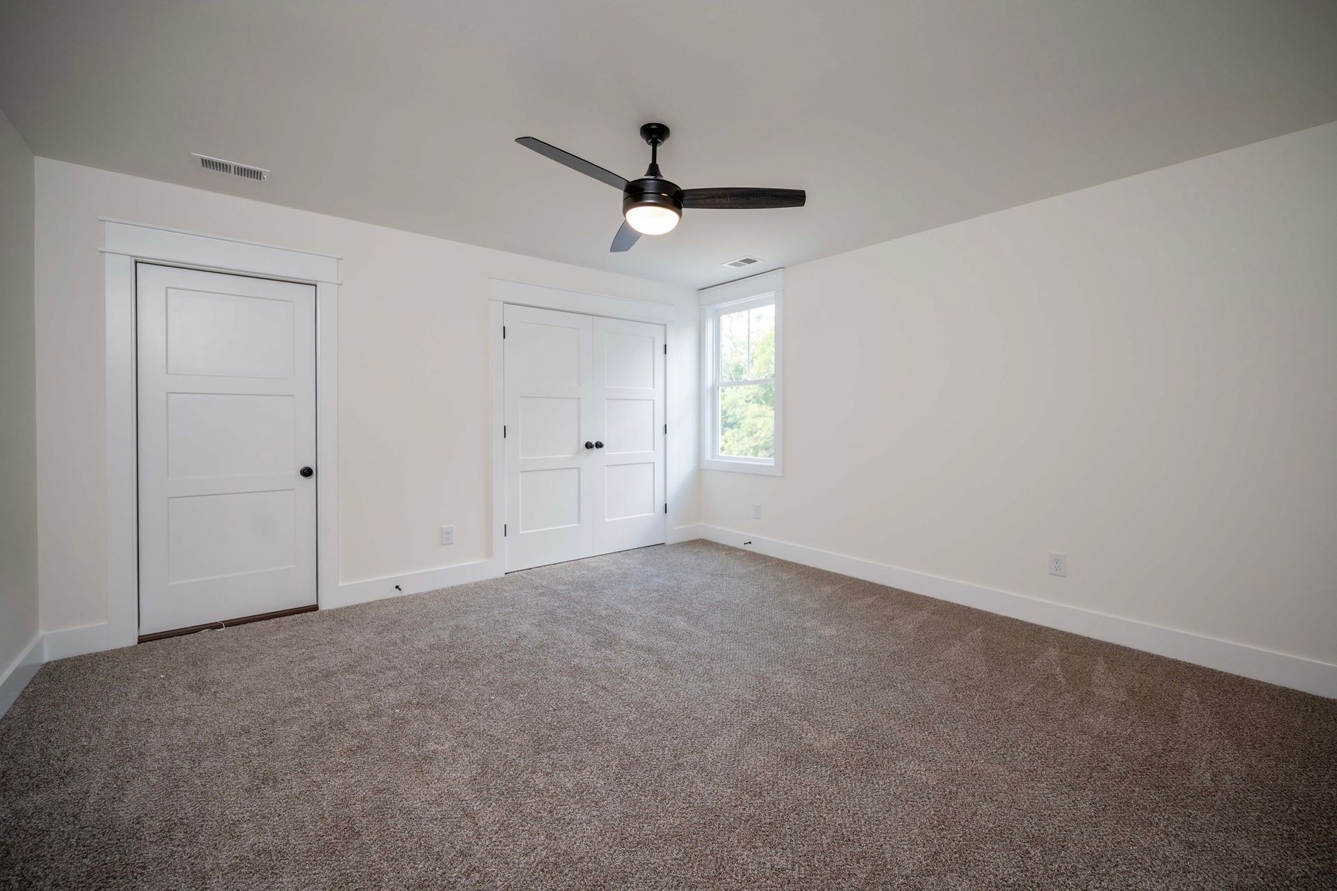 Empty bedroom with light carpet, white walls, closet, and ceiling fan.