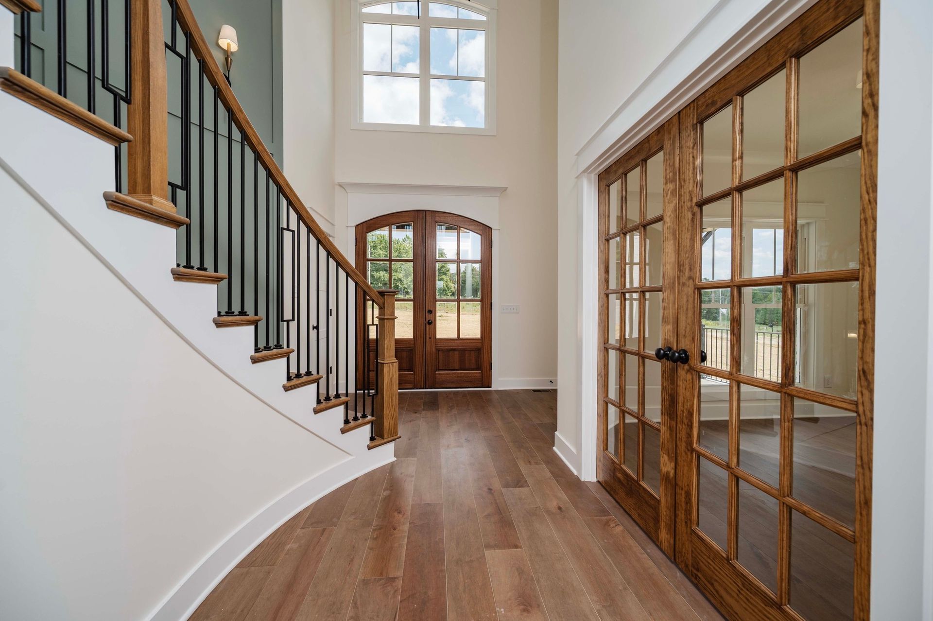 Entryway with wooden floors, staircase with black railing, and French doors.