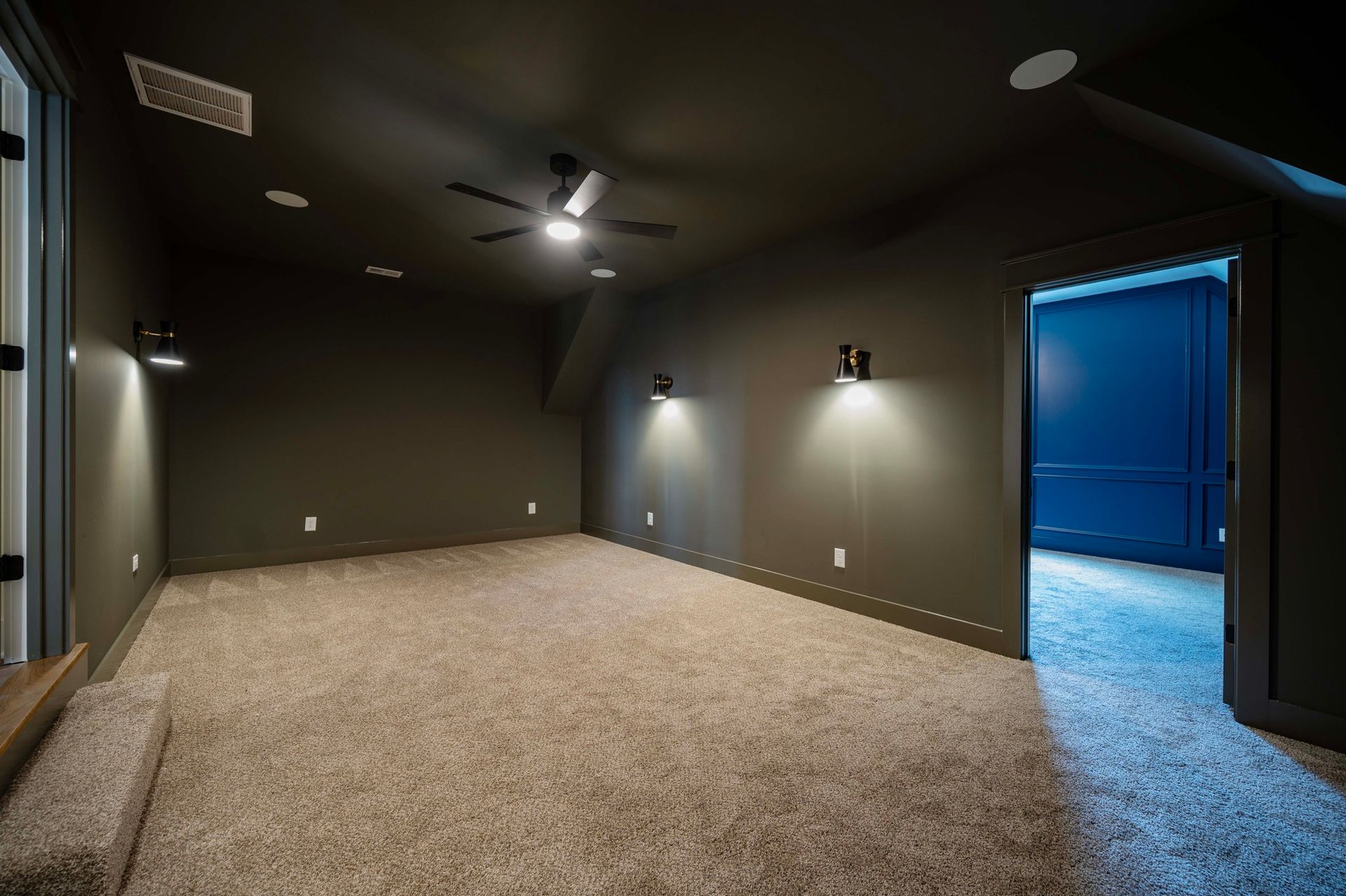 Empty, dark-walled room with beige carpet, recessed lighting, and a doorway with blue walls.