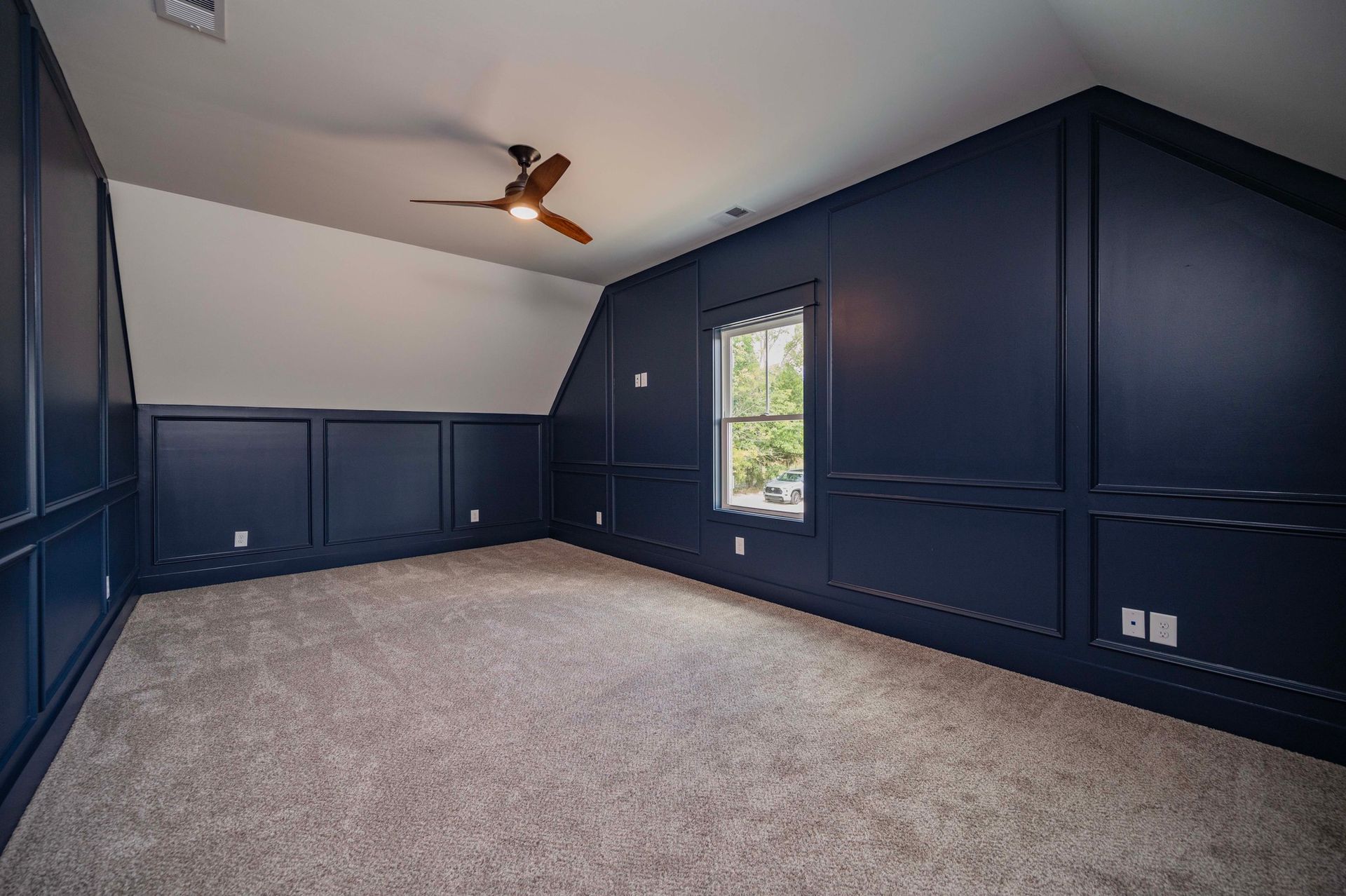 Empty room with dark blue wall paneling, beige carpet, and a ceiling fan.