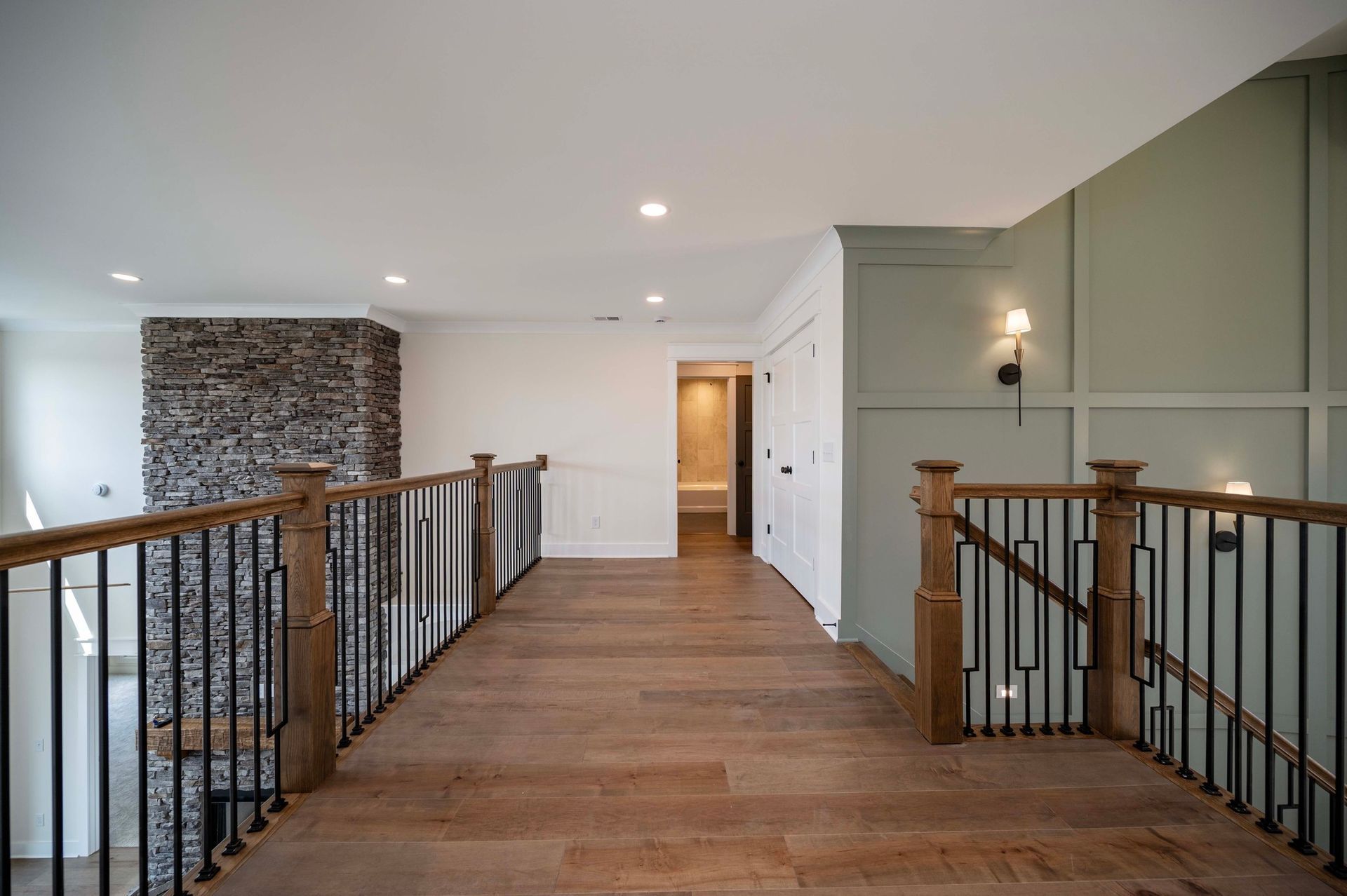 Interior hallway with wooden floor, staircase, stone wall, and light green accent wall.