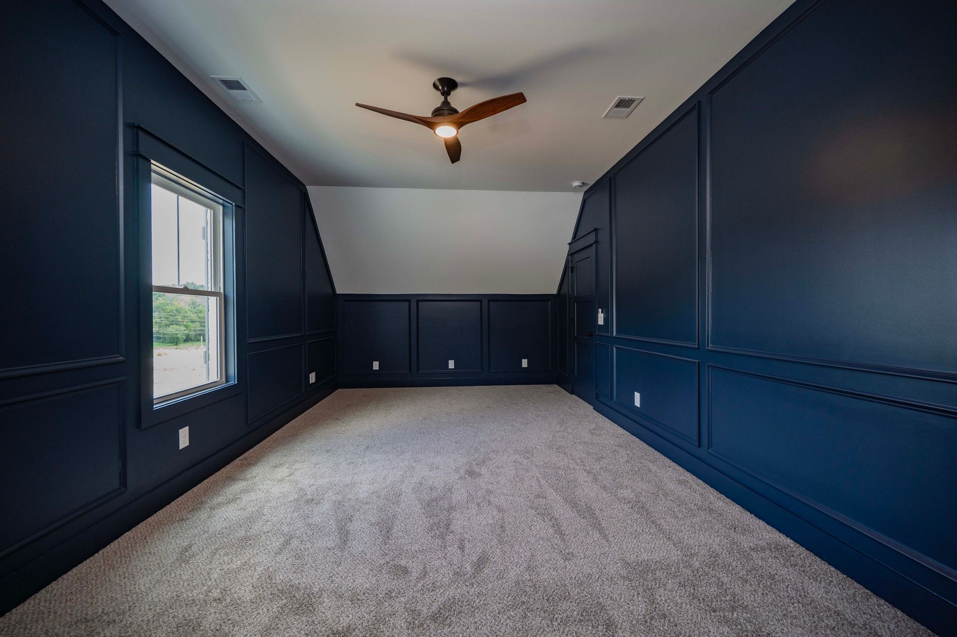 Empty room with dark blue walls, white ceiling, window, carpet, and a ceiling fan.
