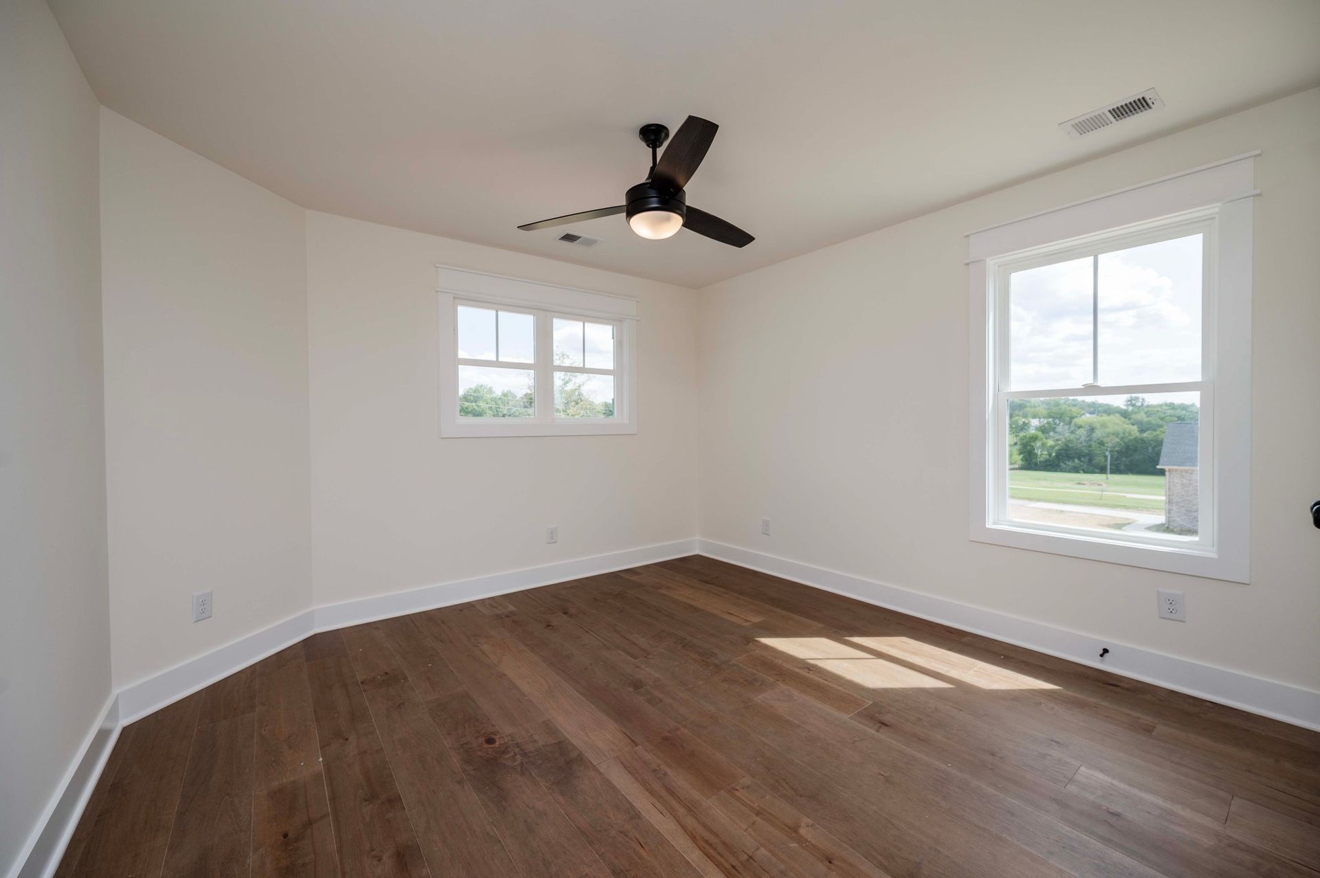 Empty room with wood floor, white walls and trim, two windows, and a ceiling fan.