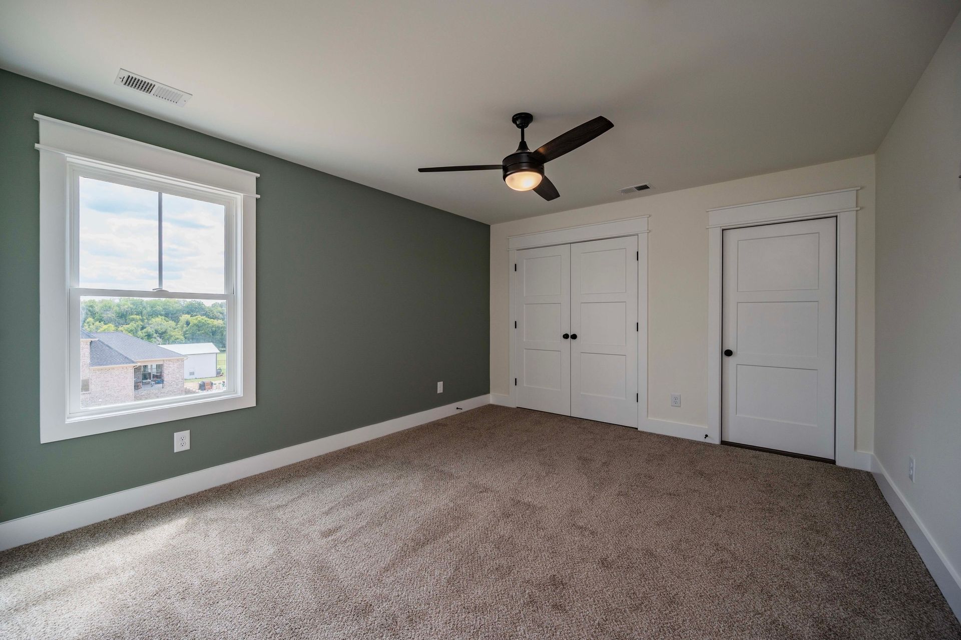Empty bedroom with green accent wall, white trim, window, closet, and ceiling fan. Carpeted floor.