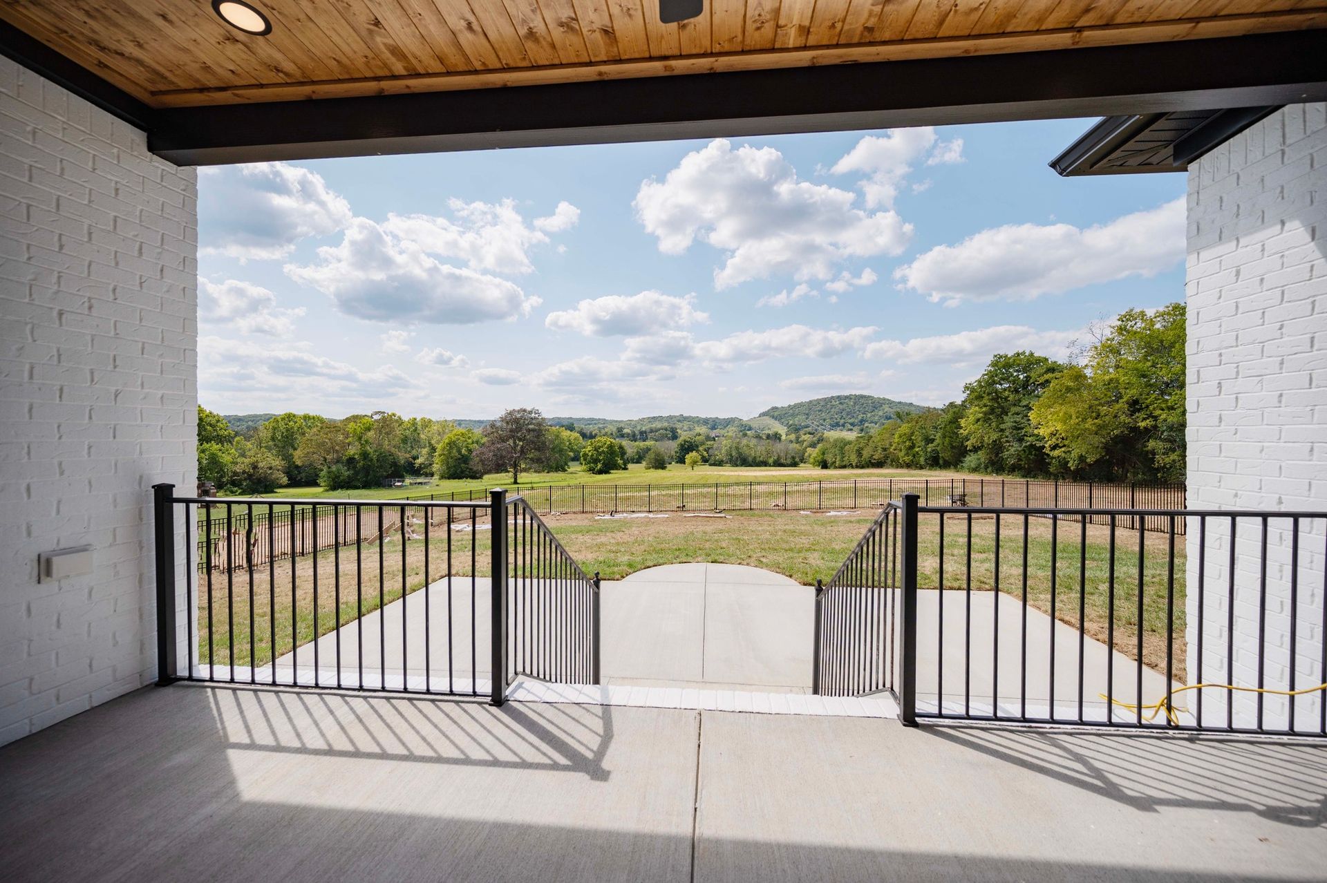 View from a covered porch looking out at a green field, blue sky with clouds.