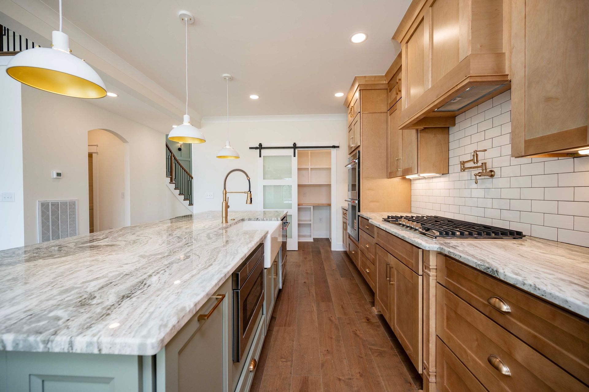 Kitchen with granite island, wooden cabinets, and pantry behind a sliding door.