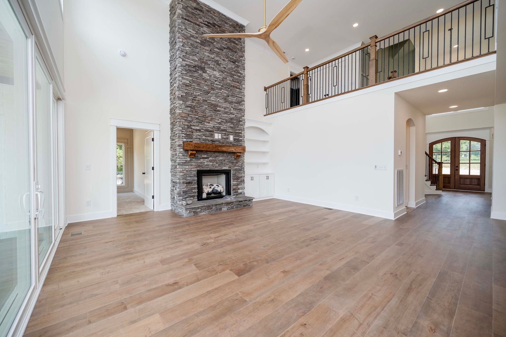 Spacious living room with stone fireplace, wooden floors, and a balcony.