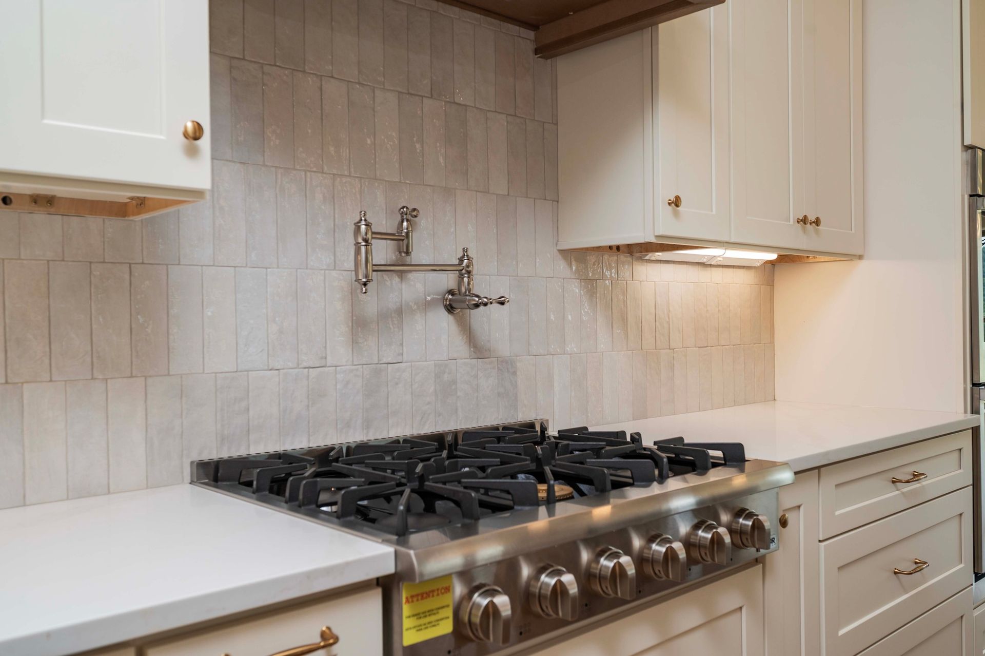 Kitchen with beige backsplash, white cabinets, stainless steel stove, and pot filler faucet.