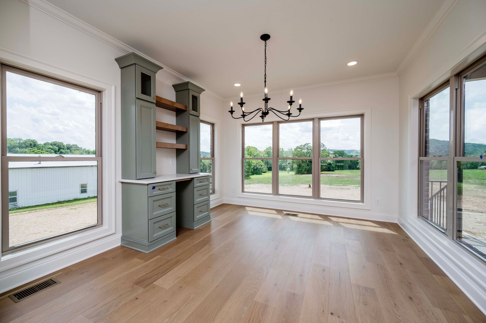 Empty room with wood floors, large windows, built-in desk and shelving, and a chandelier.