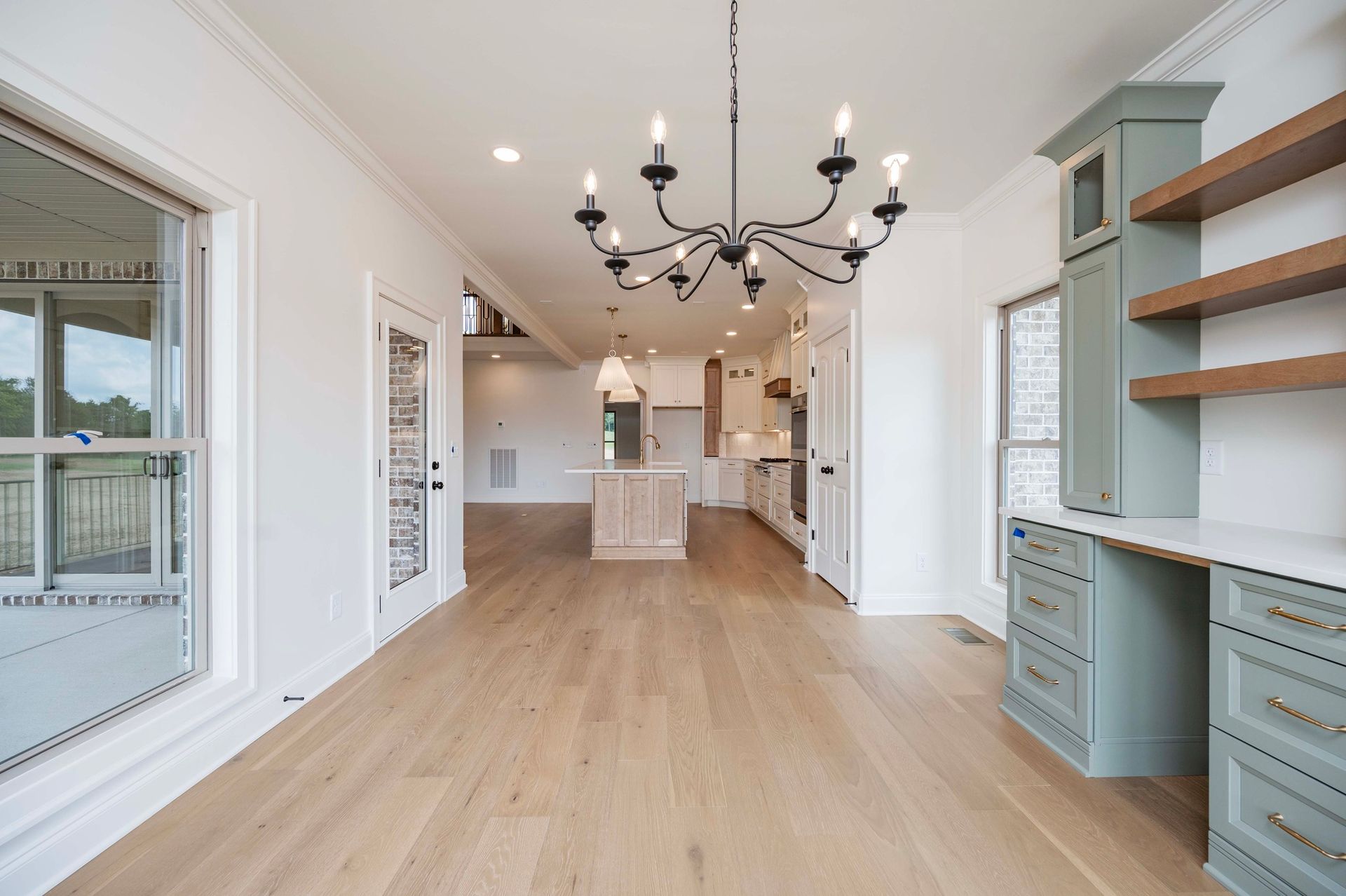 Interior view of a light-filled dining space with wooden floors, chandelier, and a built-in desk.