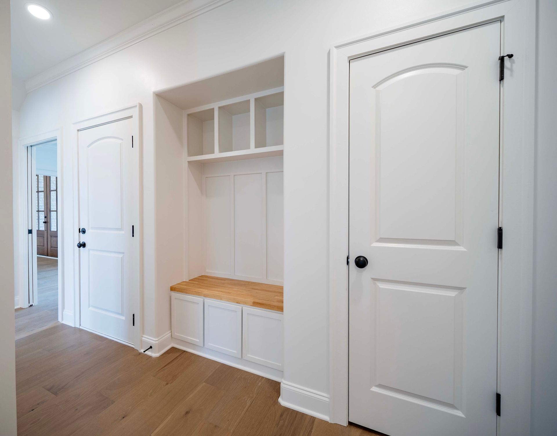 Hallway with white doors, built-in storage bench, and wood flooring.