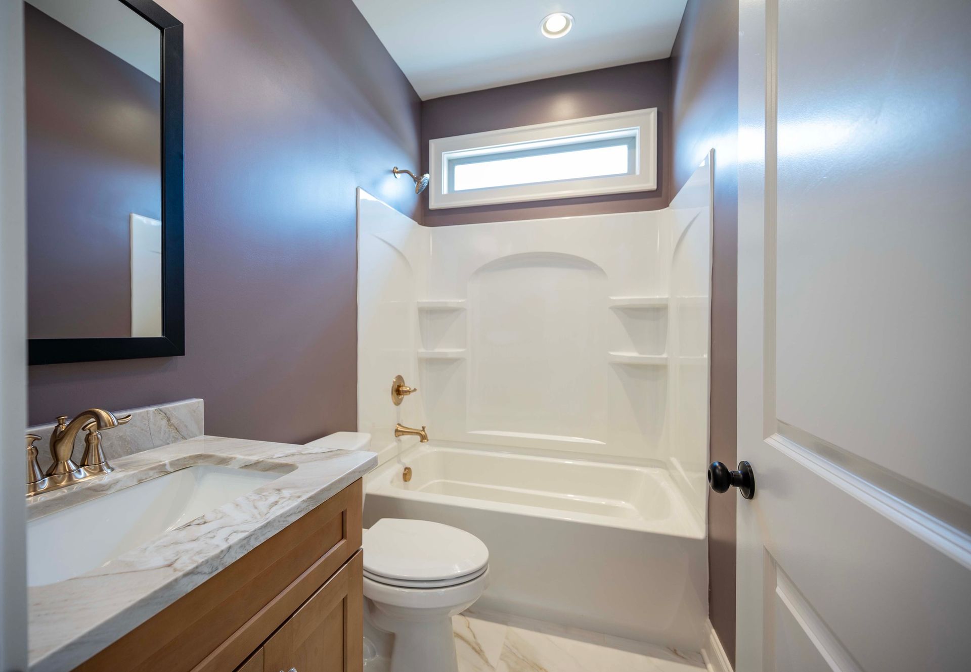 Bathroom with purple walls, white tub, toilet, vanity, and small window.