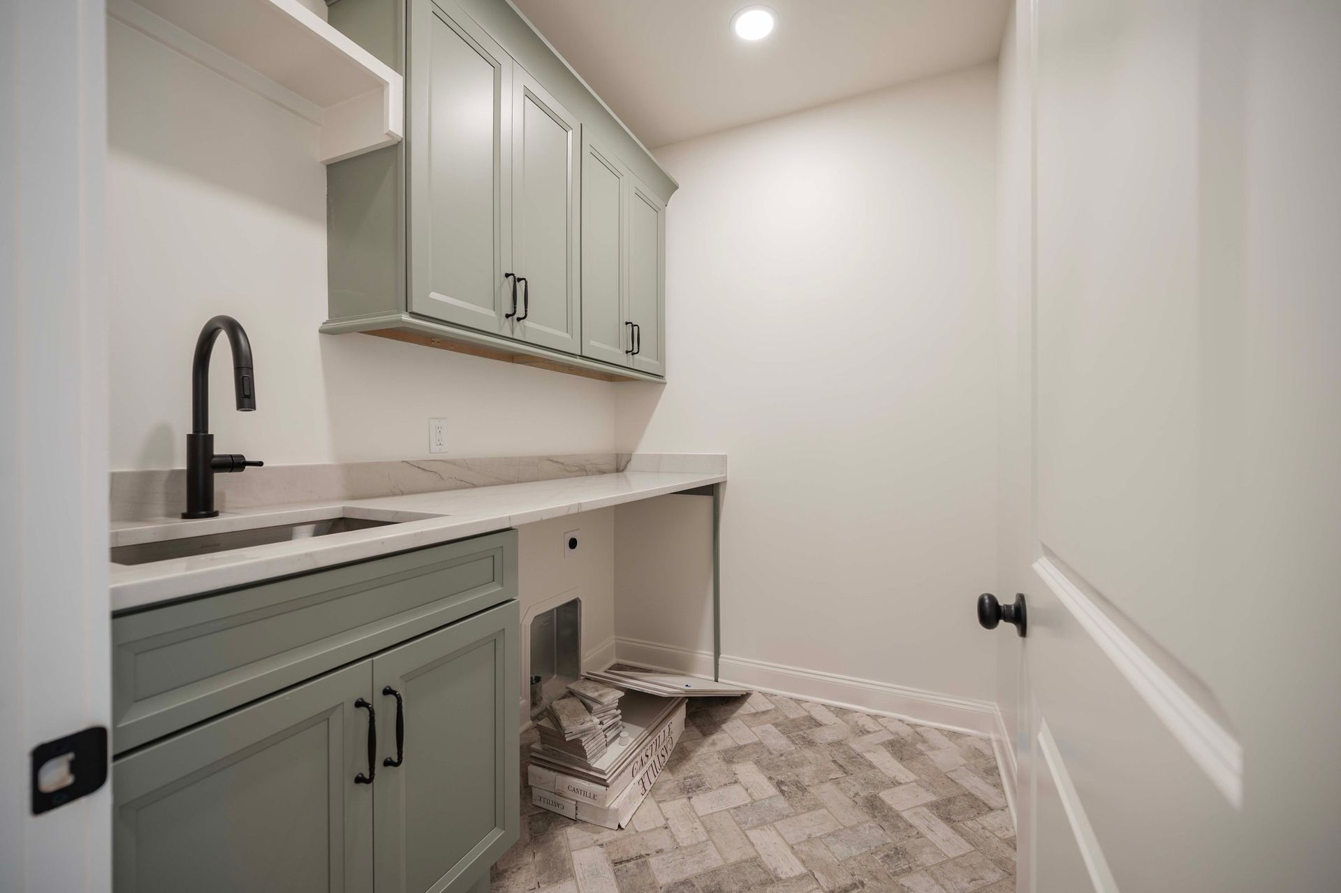 Laundry room with sage green cabinets, sink, and herringbone tile floor.