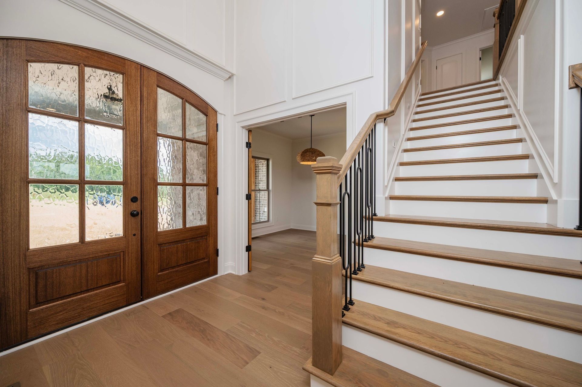 Wooden double doors and a staircase in a bright foyer.