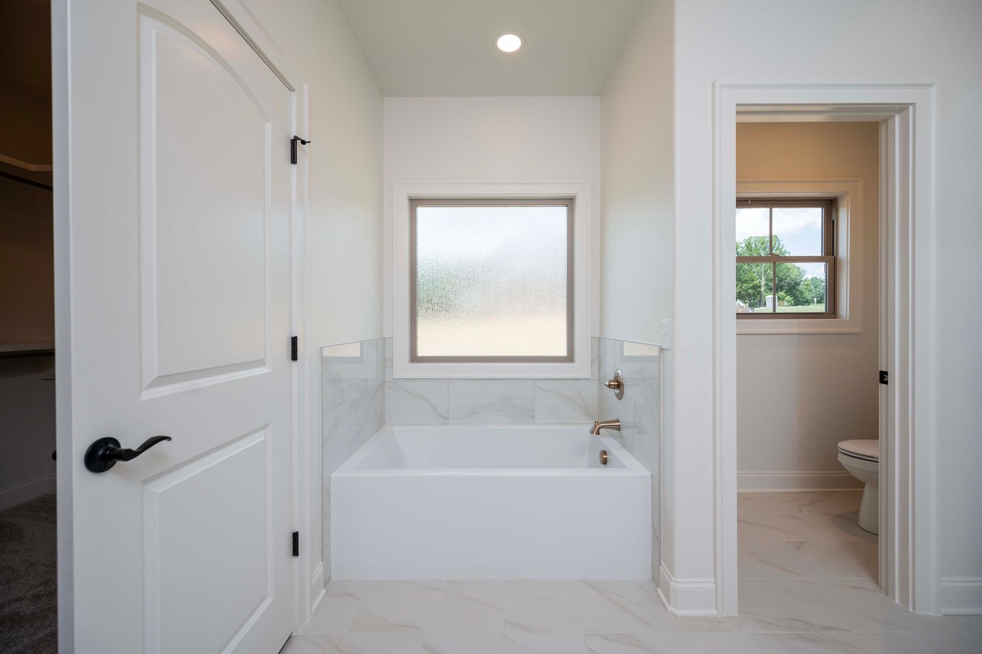 Bathroom with white tub, window, marble wall accent, and doorways.