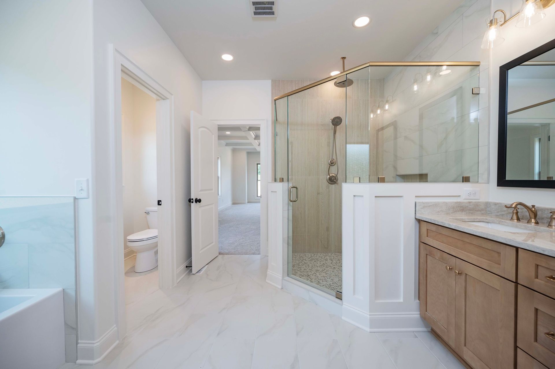 Bright, spacious bathroom with a glass shower, wooden vanity, and marble-like flooring.