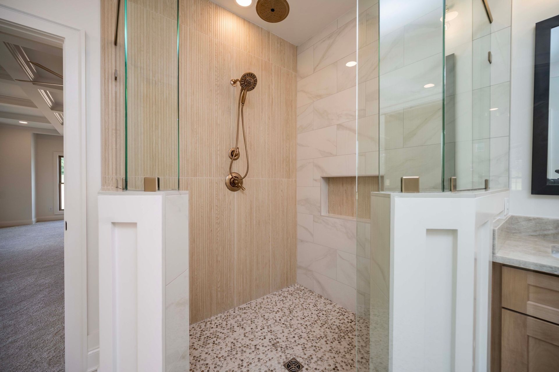 Modern bathroom with glass shower enclosure, gold fixtures, and beige tile.