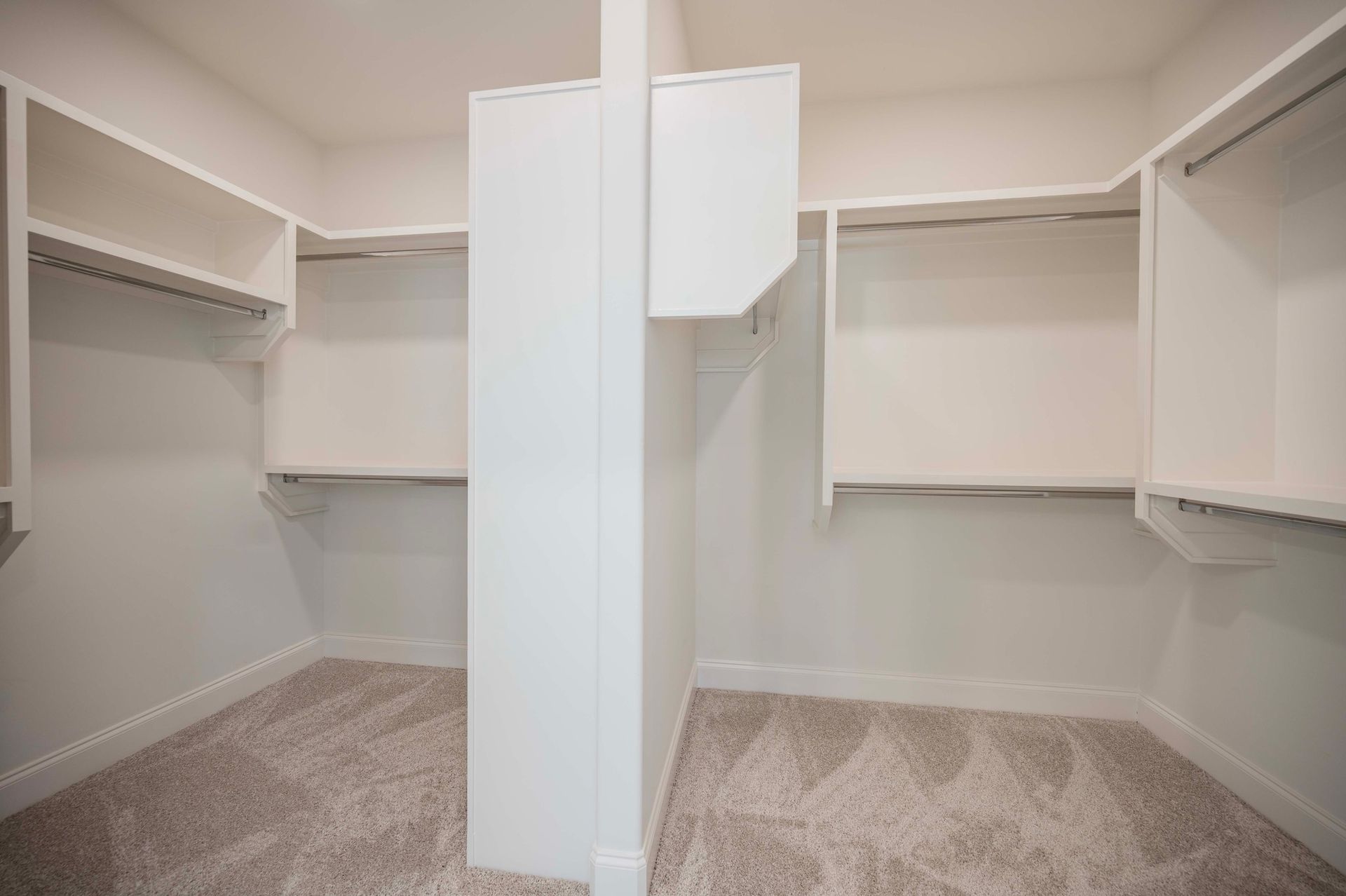 Empty white closet with shelving and hanging rods. Beige carpet.